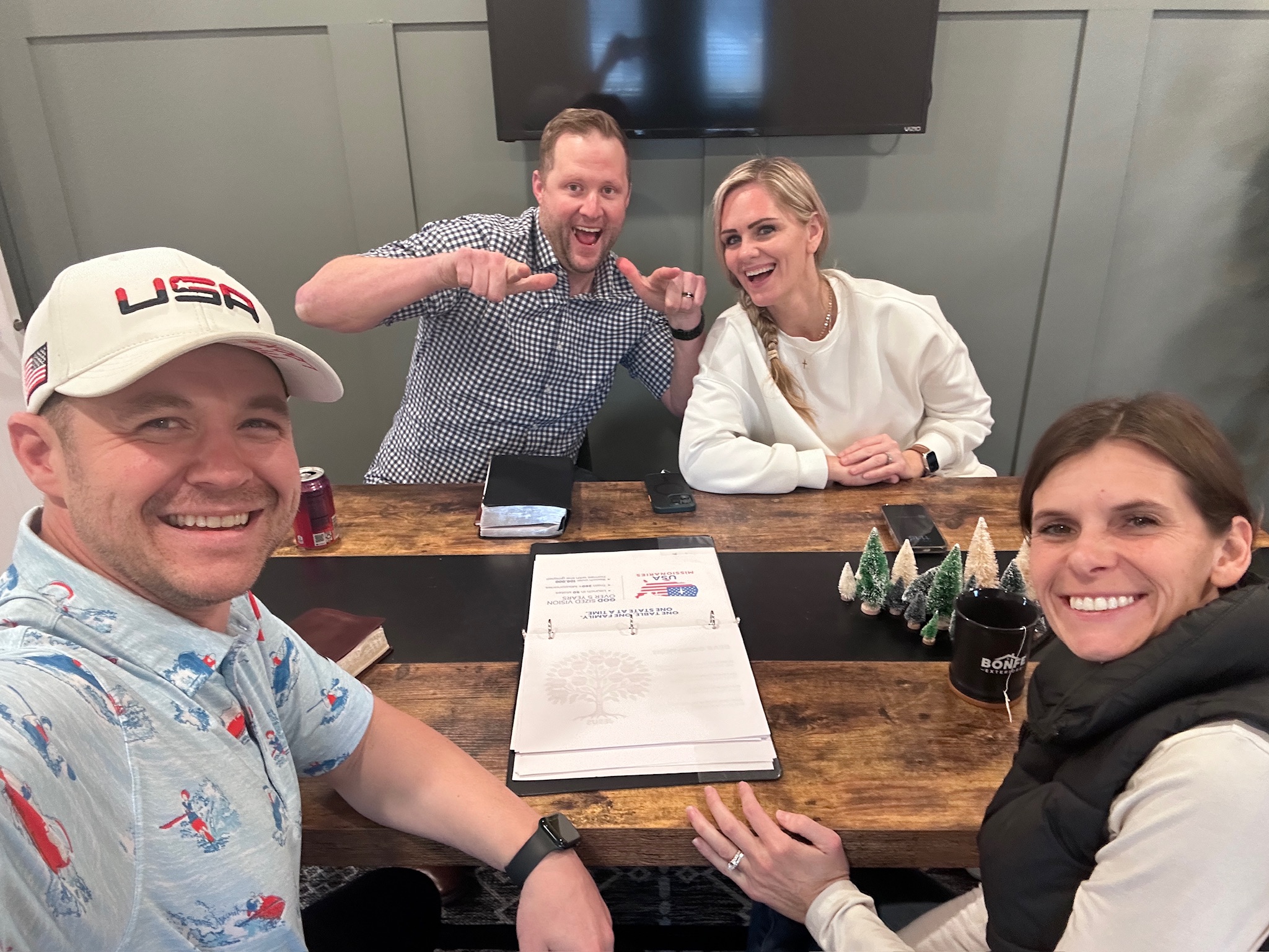 A team gathered around a wooden kitchen table with a Kitchen Table Gospel binder open